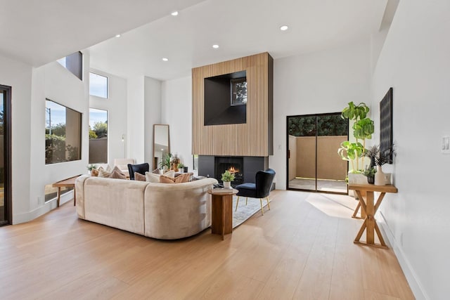 living room featuring a large fireplace, light wood-style flooring, baseboards, and recessed lighting