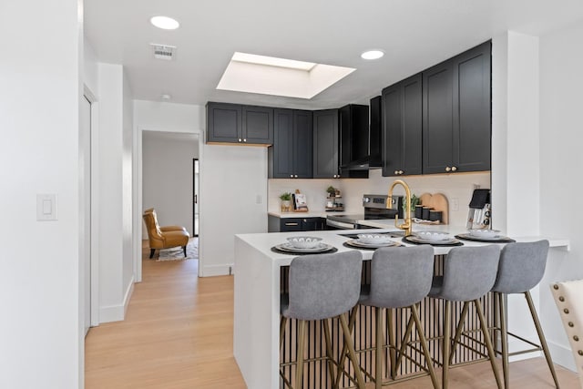 kitchen featuring visible vents, wall chimney range hood, stainless steel electric stove, light countertops, and light wood-style floors