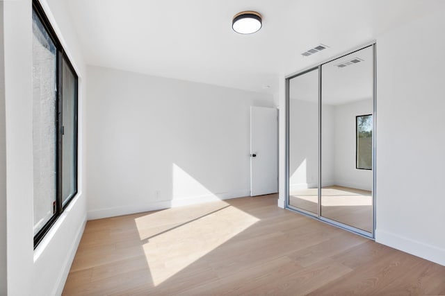 unfurnished bedroom with light wood-type flooring, baseboards, visible vents, and a closet