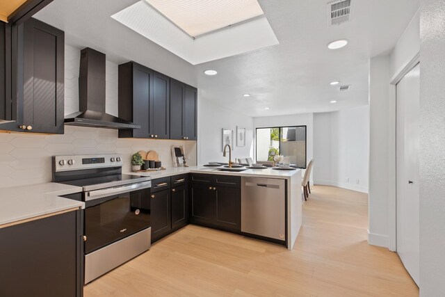 kitchen with light countertops, appliances with stainless steel finishes, a sink, a peninsula, and wall chimney exhaust hood