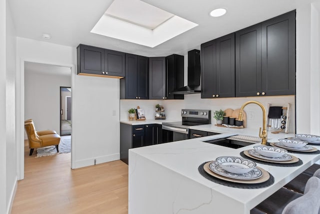 kitchen with light stone countertops, dark cabinetry, wall chimney range hood, and stainless steel electric stove