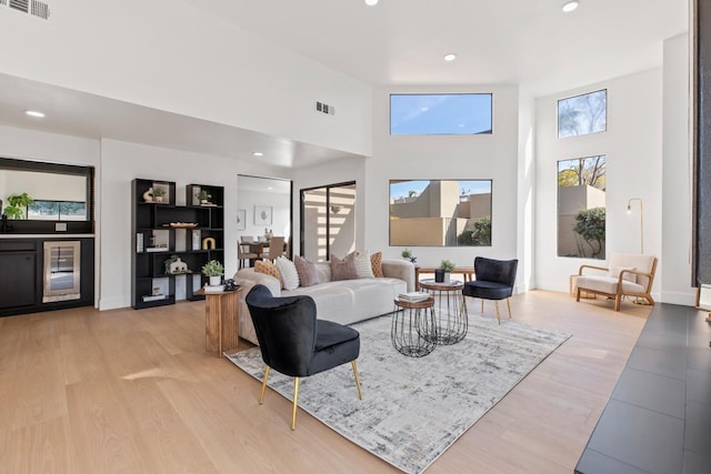 living area featuring light wood finished floors, a towering ceiling, visible vents, and recessed lighting