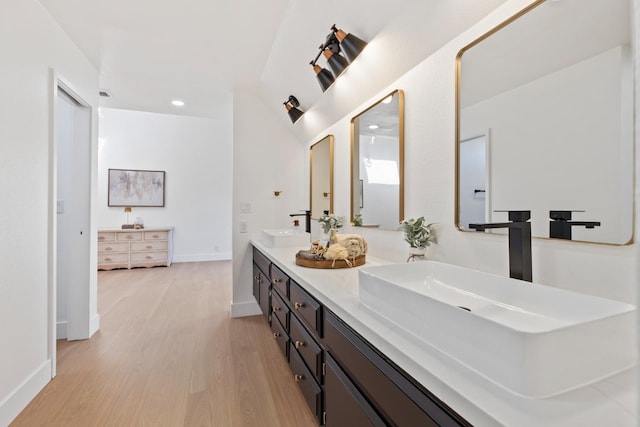 bathroom with double vanity, recessed lighting, a sink, wood finished floors, and baseboards