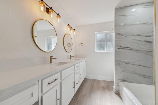 full bath with double vanity, baseboards, a sink, and wood finished floors