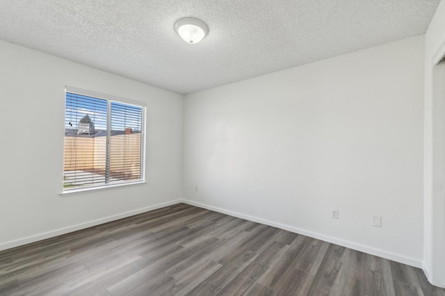 spare room featuring a textured ceiling, dark wood-type flooring, and baseboards