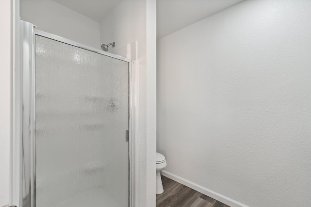 bathroom with a stall shower, baseboards, toilet, and wood finished floors