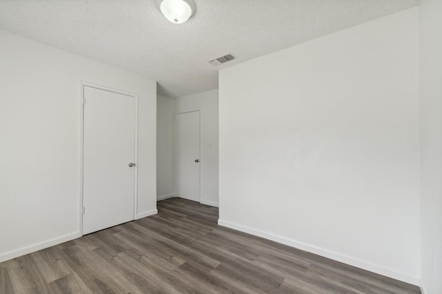 empty room with dark wood-style floors, a textured ceiling, visible vents, and baseboards