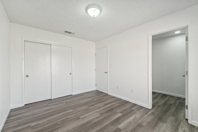 unfurnished bedroom featuring baseboards, visible vents, dark wood-type flooring, and a closet