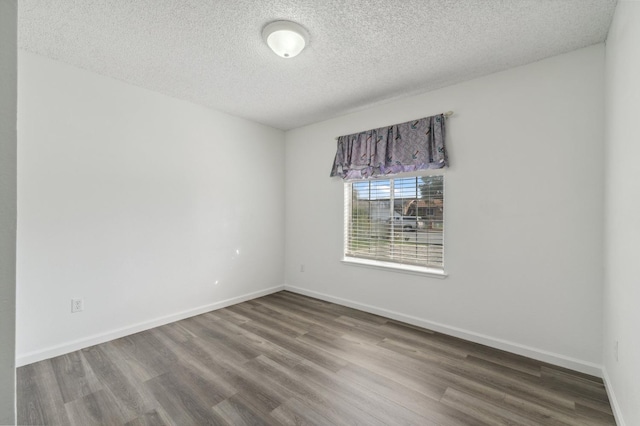 empty room with a textured ceiling, baseboards, and wood finished floors