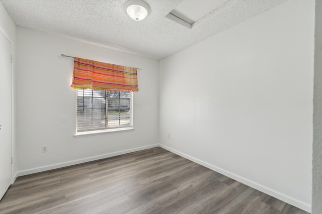 empty room with attic access, a textured ceiling, baseboards, and wood finished floors