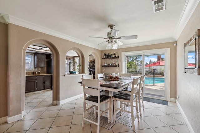 dining space with light tile patterned floors, arched walkways, visible vents, baseboards, and crown molding