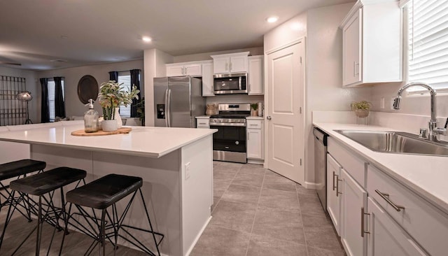 kitchen with stainless steel appliances, a breakfast bar, white cabinetry, and a sink