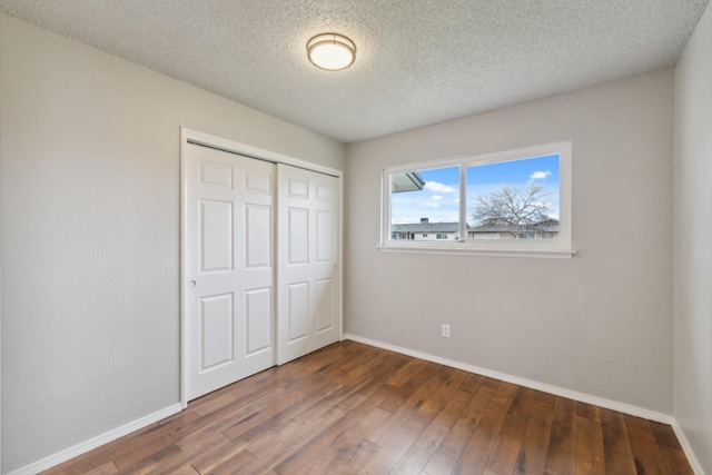 unfurnished bedroom with a closet, dark wood-style flooring, a textured ceiling, and baseboards