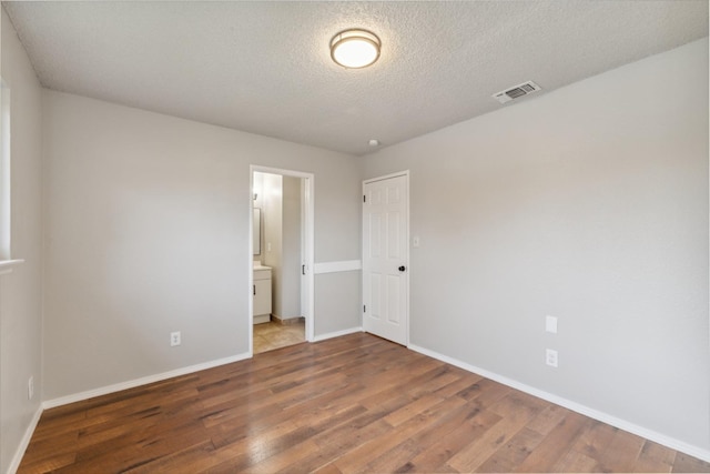 spare room with dark wood-style floors, visible vents, a textured ceiling, and baseboards