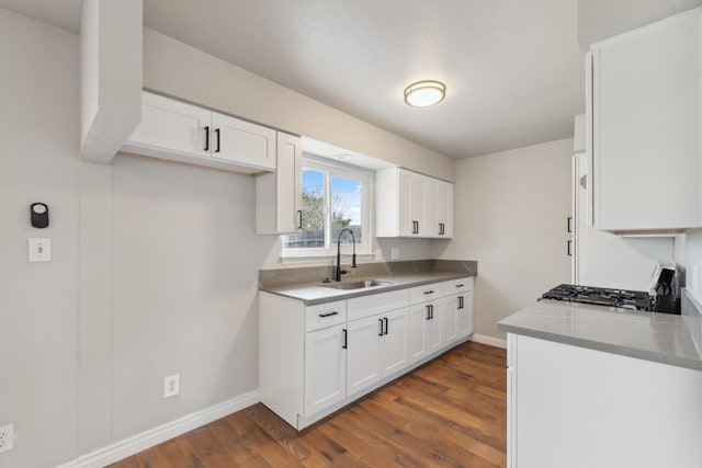 kitchen with dark wood-type flooring, white cabinetry, a sink, range, and baseboards