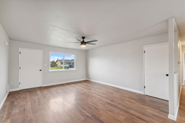 empty room with baseboards, a ceiling fan, and dark wood-type flooring