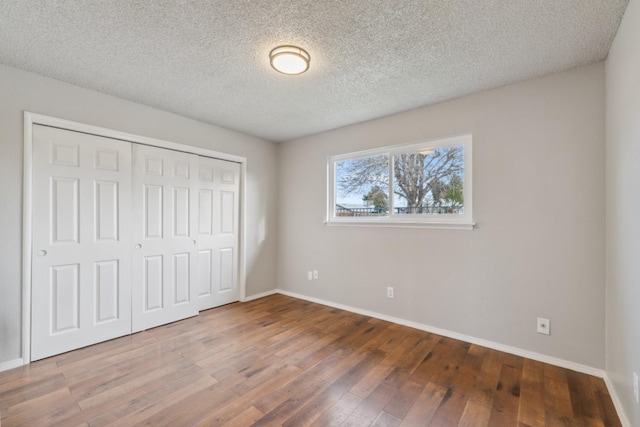 unfurnished bedroom with a textured ceiling, a closet, wood finished floors, and baseboards