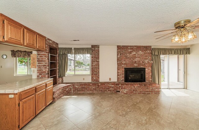 kitchen featuring brown cabinets, tile counters, a wealth of natural light, visible vents, and open floor plan