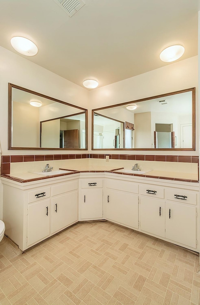 full bath featuring double vanity, a sink, visible vents, and backsplash