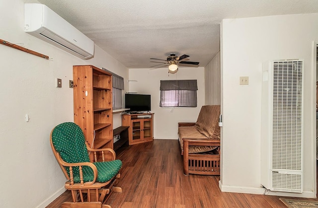 living area with a textured ceiling, a ceiling fan, a wall mounted AC, dark wood-style floors, and a heating unit