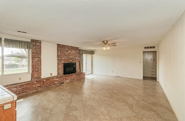 unfurnished living room with a brick fireplace, visible vents, ceiling fan, and a textured ceiling