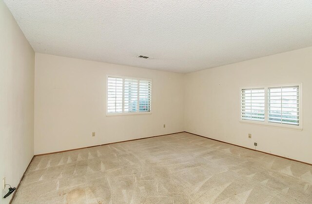 unfurnished room with light carpet, visible vents, and a textured ceiling