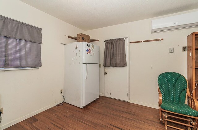 interior space featuring a wall mounted AC, baseboards, dark wood-type flooring, and freestanding refrigerator