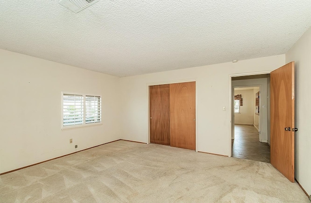 unfurnished bedroom with light tile patterned floors, a closet, visible vents, light carpet, and a textured ceiling