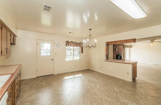 unfurnished dining area featuring a fireplace, light tile patterned floors, visible vents, baseboards, and ceiling fan with notable chandelier