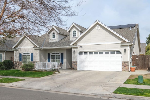 view of front of home with driveway, a garage, solar panels, stone siding, and fence