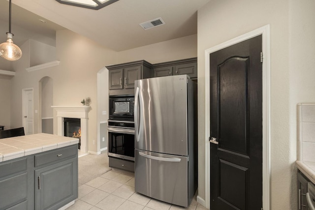 kitchen featuring pendant lighting, tile countertops, visible vents, appliances with stainless steel finishes, and a glass covered fireplace