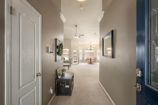 corridor with baseboards, a textured wall, ornamental molding, carpet, and a chandelier