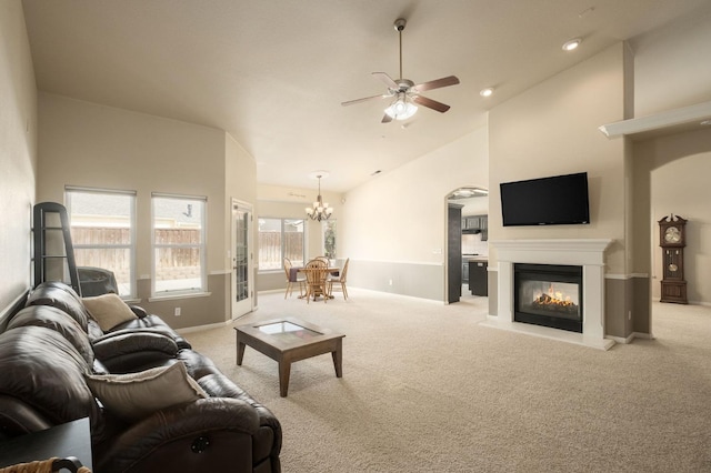 living room featuring light colored carpet, a multi sided fireplace, high vaulted ceiling, baseboards, and ceiling fan with notable chandelier