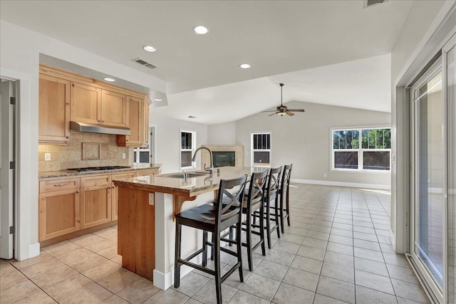 kitchen with light stone countertops, a kitchen island with sink, light brown cabinetry, a kitchen bar, and a sink