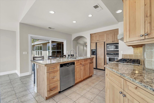 kitchen featuring stainless steel appliances, a sink, a center island with sink, and light stone counters