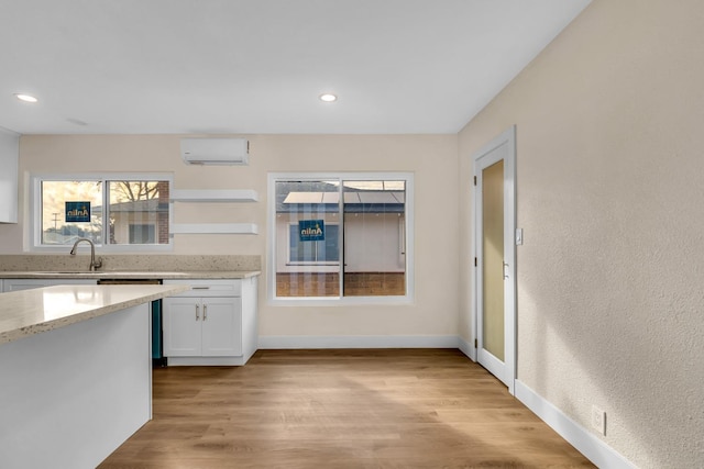 506 W Terrace Ave, Fresno, CA 93705 - kitchen featuring a wall unit AC, white cabinets, light stone countertops, light wood-type flooring, and baseboards