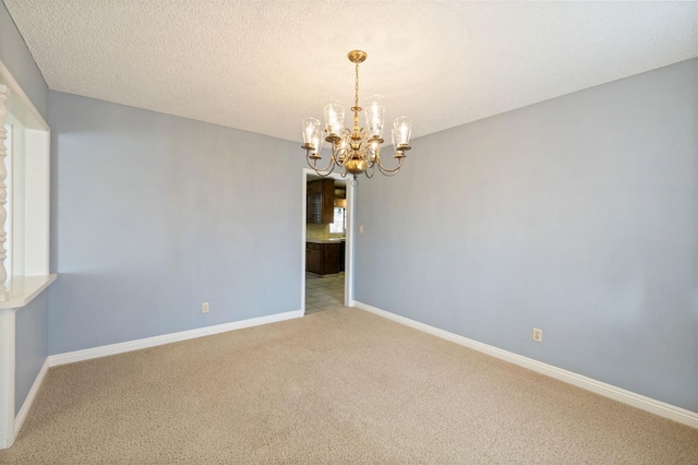 carpeted spare room featuring a chandelier, a textured ceiling, and baseboards