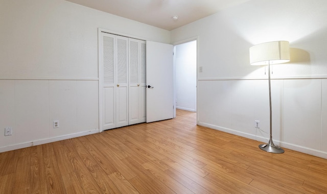 unfurnished bedroom featuring light wood-style floors, a closet, and a wainscoted wall