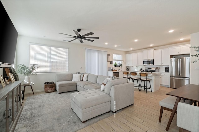 living area featuring light wood-style flooring, baseboards, a ceiling fan, and recessed lighting