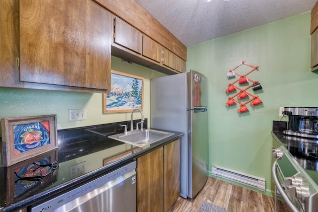 kitchen with appliances with stainless steel finishes, brown cabinets, baseboard heating, and a sink