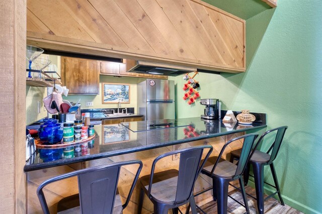 bar with a sink, a textured wall, freestanding refrigerator, black electric cooktop, and extractor fan