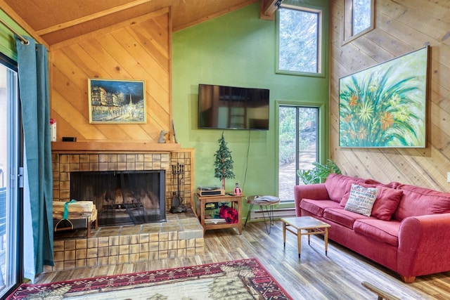 living room featuring high vaulted ceiling, wood walls, wood finished floors, and a tile fireplace