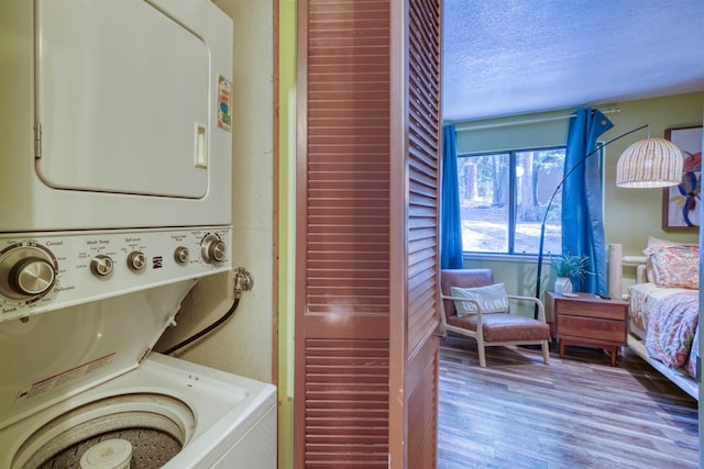 laundry area featuring wood finished floors, a textured ceiling, stacked washer / drying machine, and laundry area