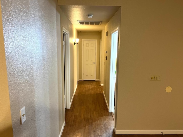 hallway featuring dark wood-type flooring, visible vents, and baseboards