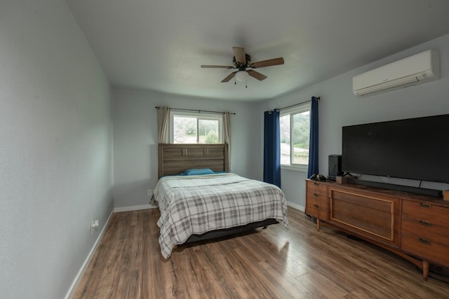 bedroom featuring ceiling fan, baseboards, wood finished floors, and a wall mounted air conditioner