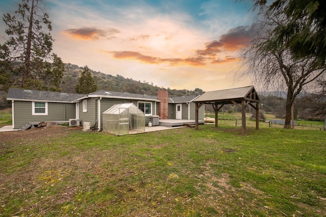 back of property at dusk with an outbuilding, a gazebo, a lawn, ac unit, and an exterior structure