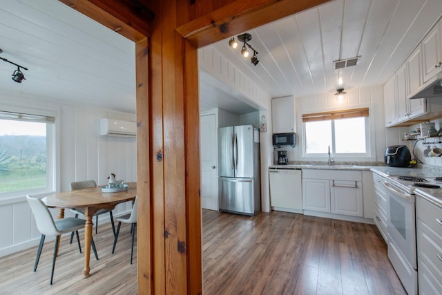 kitchen with a wealth of natural light, white appliances, white cabinets, and a wall mounted air conditioner