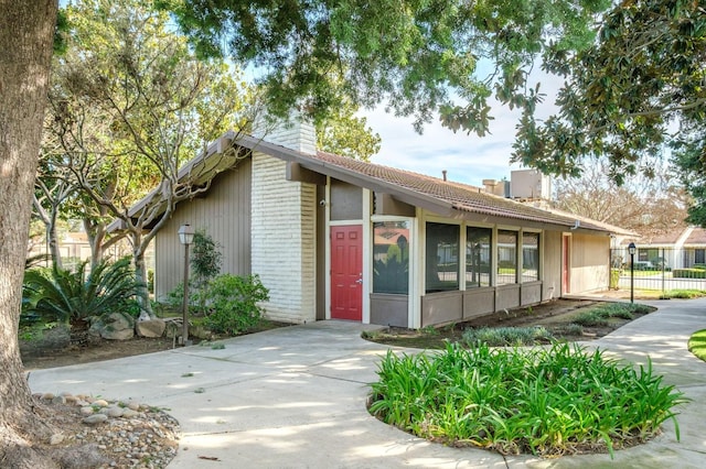 mid-century home featuring a sunroom, brick siding, fence, and a chimney