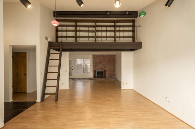 unfurnished living room with a brick fireplace, a high ceiling, visible vents, and wood finished floors