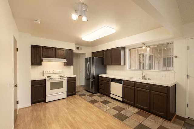 kitchen with dark brown cabinetry, white appliances, light countertops, under cabinet range hood, and a sink